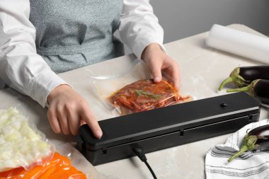 Woman using sealer for vacuum packing on white marble table, closeup