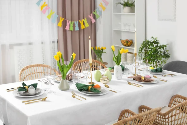 stock image Festive Easter table setting with painted eggs, burning candles and yellow tulips in room