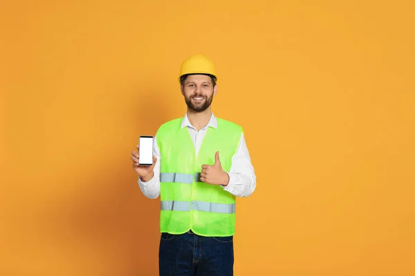 stock image Man in reflective uniform showing smartphone and thumbs up on orange background