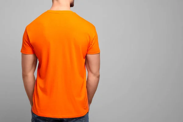 Man wearing orange t-shirt on light grey background, back view. Mockup for design