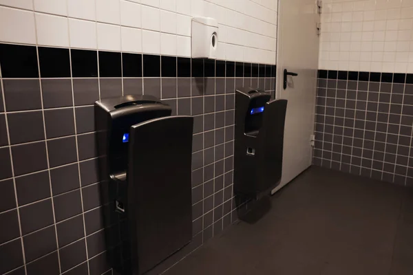 Modern hand dryers on tiled wall in public toilet