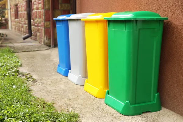 Many colorful recycling bins near brown wall outdoors