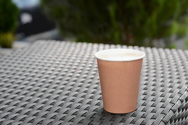Coffee cardboard cup on rattan table outdoors, space for text