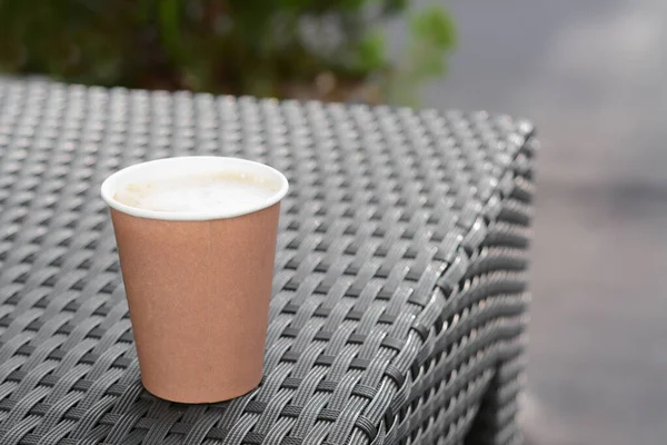 Cardboard cup with coffee on rattan table outdoors, space for text