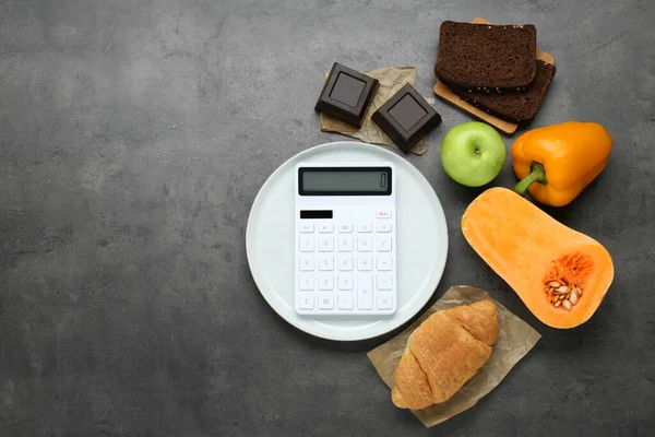 Calculator and food products on dark grey table, flat lay with space for text. Weight loss concept