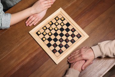 Man playing checkers with woman at wooden table, above view