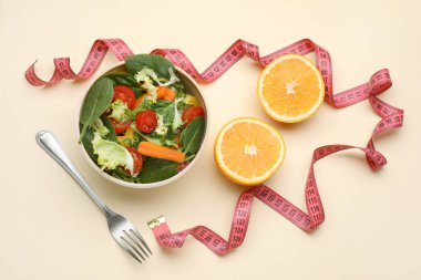 Ölçüm bandı, salata, turuncu yarımlar ve sarı arka planda çatal, düz uzanma