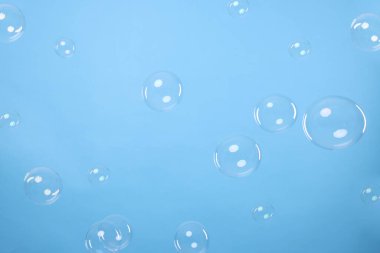 Many beautiful soap bubbles on light blue background