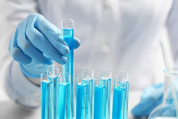 Scientist taking test tube with light blue liquid at table, closeup