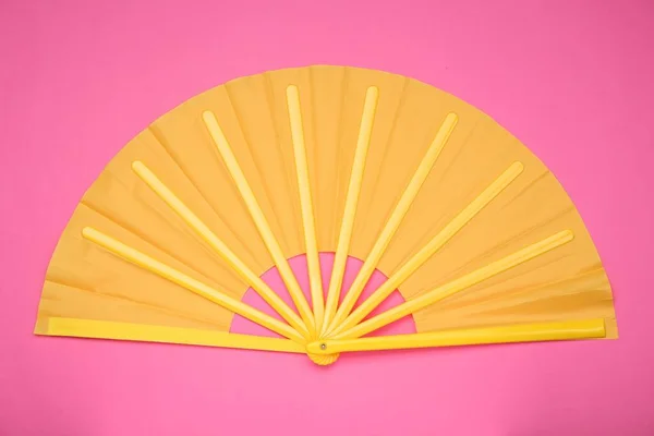 Stock image Bright yellow hand fan on pink background, top view