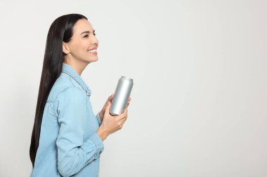 Beautiful happy woman holding beverage can on light grey background. Space for text