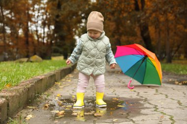 Cute little girl standing in puddle near colorful umbrella outdoors