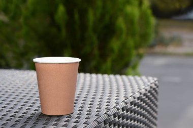 Coffee cardboard cup on rattan table outdoors, space for text
