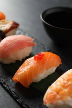 Serving board with delicious nigiri sushi and soy sauce on black table, closeup