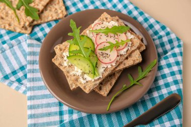 Krem peynirli gevrek, salatalık, turp ve roka bej masada servis edilir.