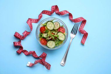 Açık mavi zemin üzerinde mezura, salata ve çatal, düz uzanma