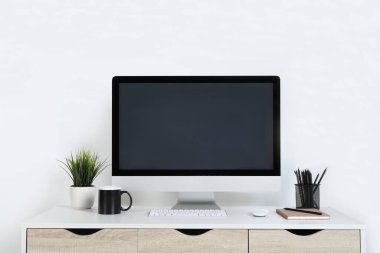 Evdeki ahşap masada bilgisayar, ev bitkisi ve kırtasiye malzemesi olan rahat çalışma alanı