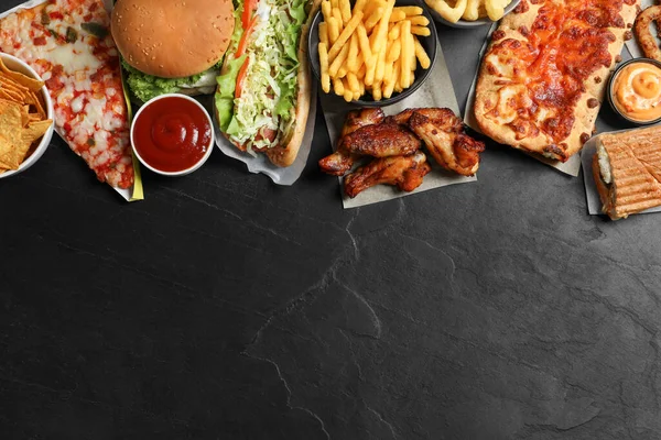 Burger, pizza and other fast food on black table, flat lay with space for text