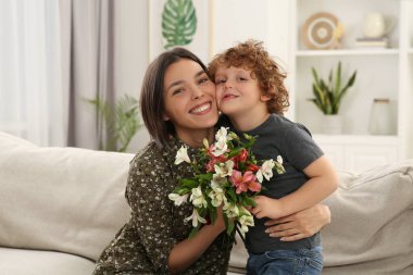 Happy woman with her cute son and bouquet of beautiful flowers at home. Mother's day celebration