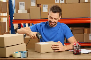 Post office worker with scanner reading parcel barcode at counter indoors