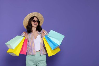Beautiful young woman with paper shopping bags on purple background. Space for text