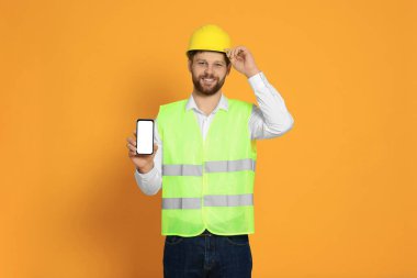 Yansıtıcı üniformalı adam turuncu arka planda akıllı telefon gösteriyor.
