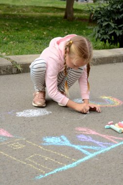 Little child drawing white clouds with chalk on asphalt