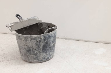 Bucket of adhesive mix and spatula on floor indoors, space for text. Tiles installation process