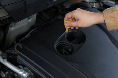 Arabadaki motor yağı seviyesini dipstick ile kontrol eden adam, yakın plan.