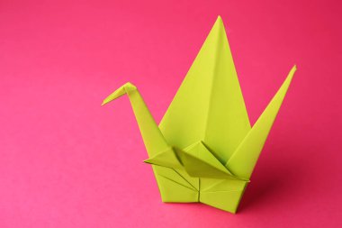 Origami art. Handmade paper crane on pink background, closeup. Space for text