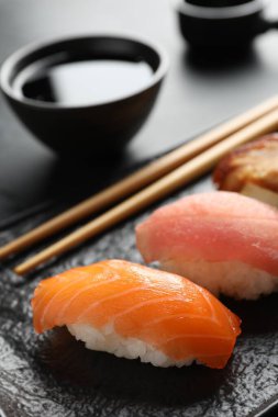 Serving board with delicious nigiri sushi and soy sauce on black table, closeup