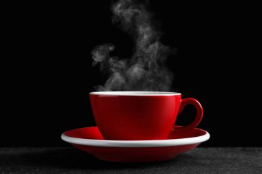 Red cup with hot steaming coffee on dark table against black background clipart