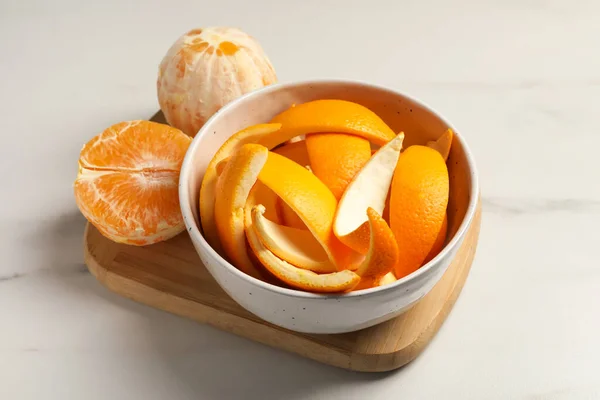 Peeled fresh fruits with orange zest preparing for drying on white marble table, closeup