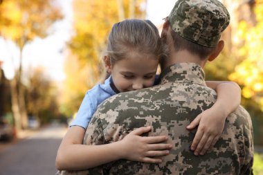 Daughter hugging her father in Ukrainian military uniform on city street. Family reunion