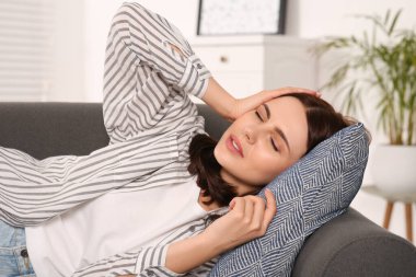 Kanepede yatarken baş ağrısı çeken genç bir kadın. Hormonal bozukluklar
