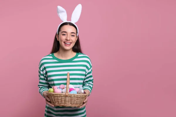 快乐的女人 戴着兔子耳朵的头巾 手里拿着一篮粉红色背景的彩绘复活节彩蛋 案文的篇幅 — 图库照片