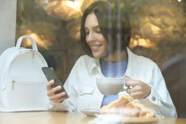 Özel terfi. Kafede akıllı telefon kullanan, bardakta içki içen mutlu genç bir kadın.