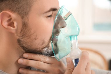 Hasta adam kapalı alanda nefes almak için nebulizör kullanıyor.