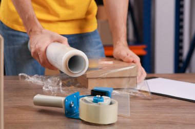 Post office worker wrapping parcel in stretch film at counter indoors, closeup