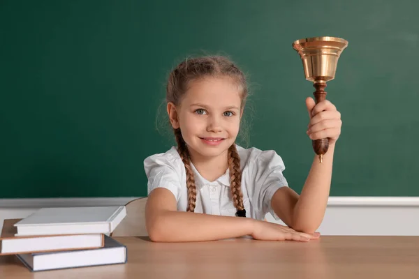 Pupil with school bell sitting at desk near chalkboard in classroom