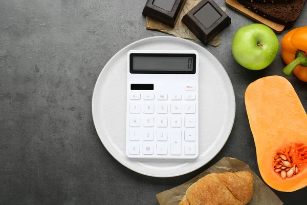 Calculator and food products on dark grey table, flat lay with space for text. Weight loss concept