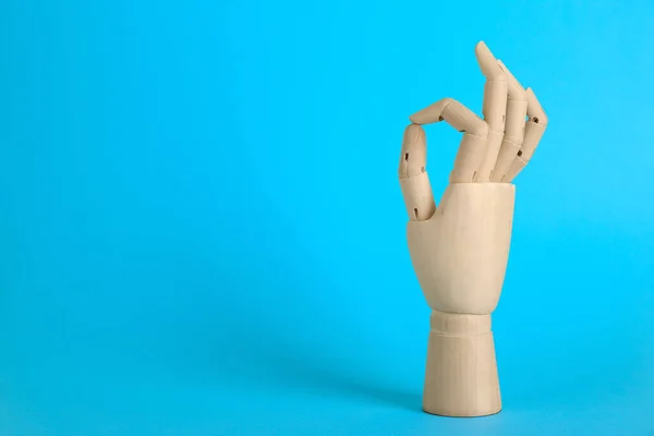 Wooden mannequin hand showing okay gesture on light blue background. Space for text