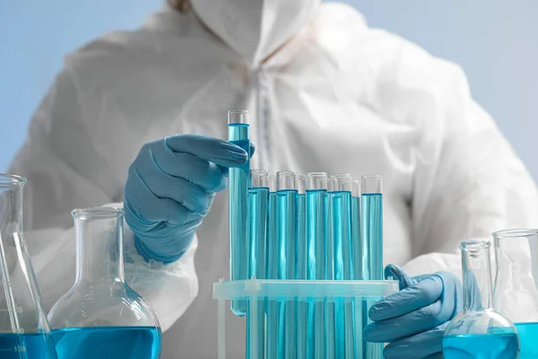 Scientist taking test tube with light blue liquid on grey background, closeup