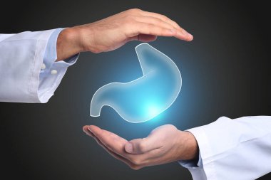 Mide ekşimesinin ve diğer gastrointestinal hastalıkların semptomları. Siyah arka planda mide illüstrasyonunu tutan doktor, yakın plan.
