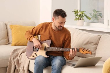 Evde online müzik kursuyla gitar çalmayı öğrenen bir adam. Hobi zamanı.