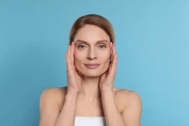 Woman massaging her face on turquoise background