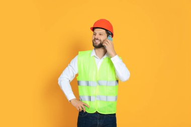 Man in reflective uniform talking on smartphone against orange background