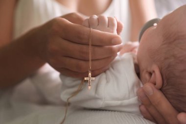 Hristiyan haçı tutan anne yeni doğmuş bebeğin yanında, kapalı yerde, yakın plan.