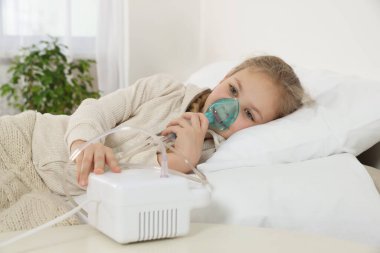 Evdeki yatakta nebulizör kullanan küçük kız.