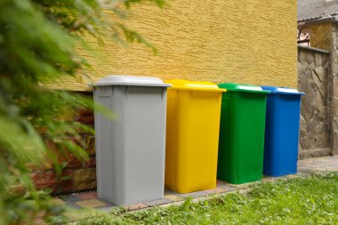 Many colorful recycling bins near yellow wall outdoors